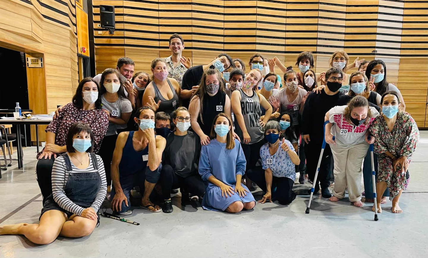 A group of people indoors. Some are using mobility aids. They are wearing comfortable gym clothes and face masks.